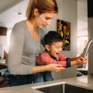 woman holds boy to wash hands at sink 