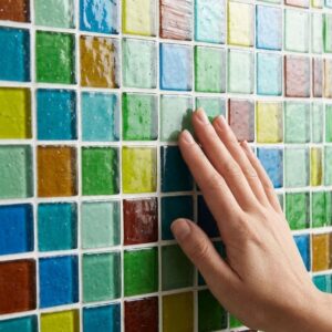 A hand explores the texture of a colorful recycled glass tile bathroom mosaic.