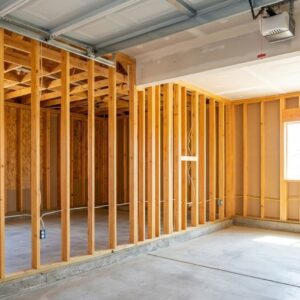 A residential garage interior shows new wooden wall framing installed for a conversion project.